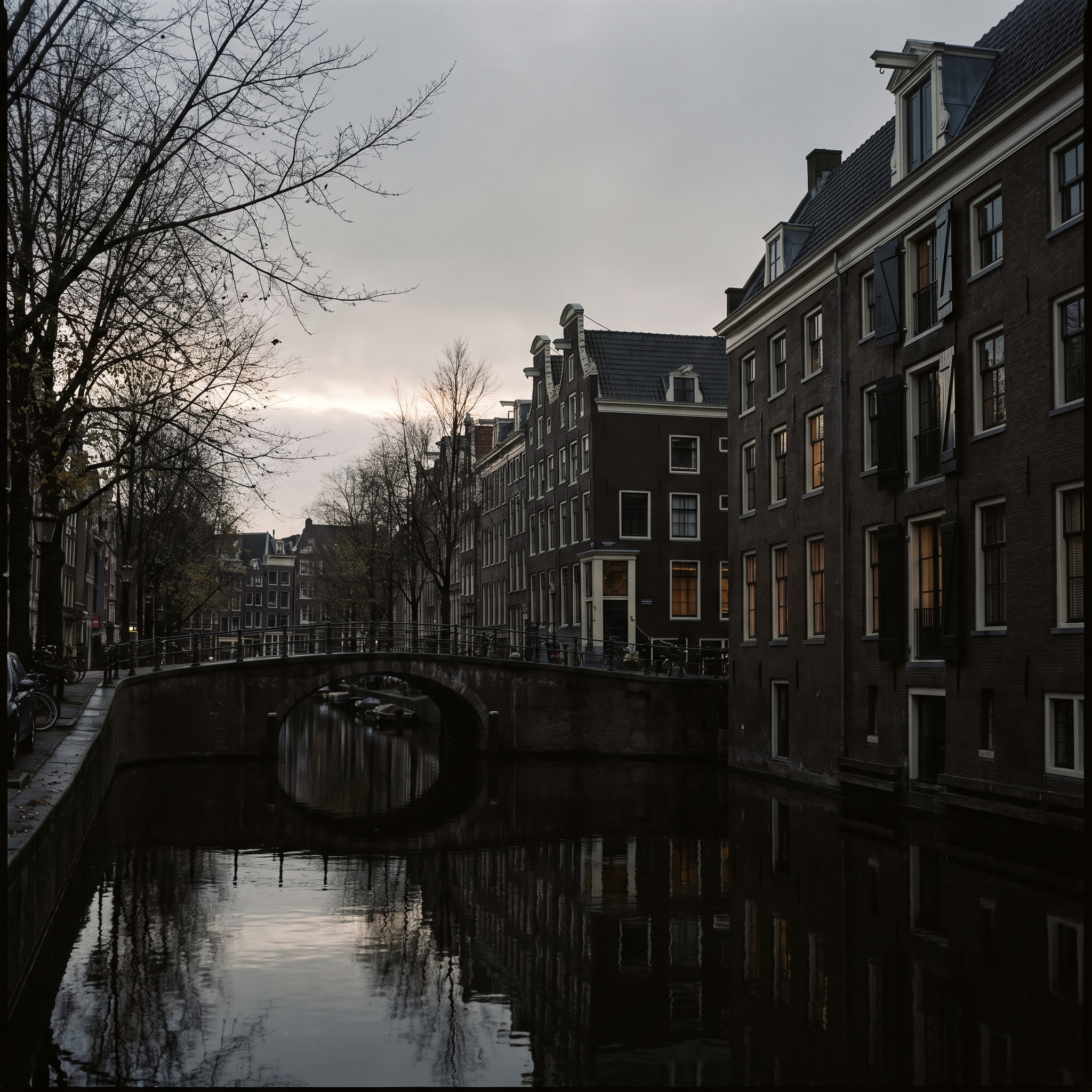 An Amsterdam canal in flat grey October light, dark brick fronts and black water