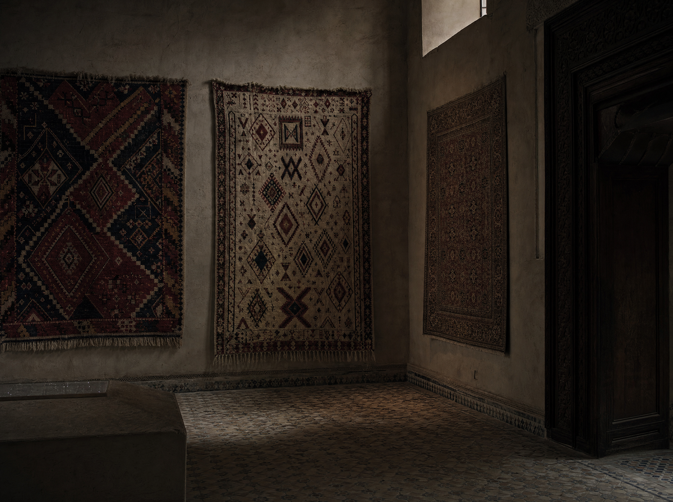 Moroccan carpets hung flat on plain plaster: two High Atlas weavings beside a finer urban floral carpet
