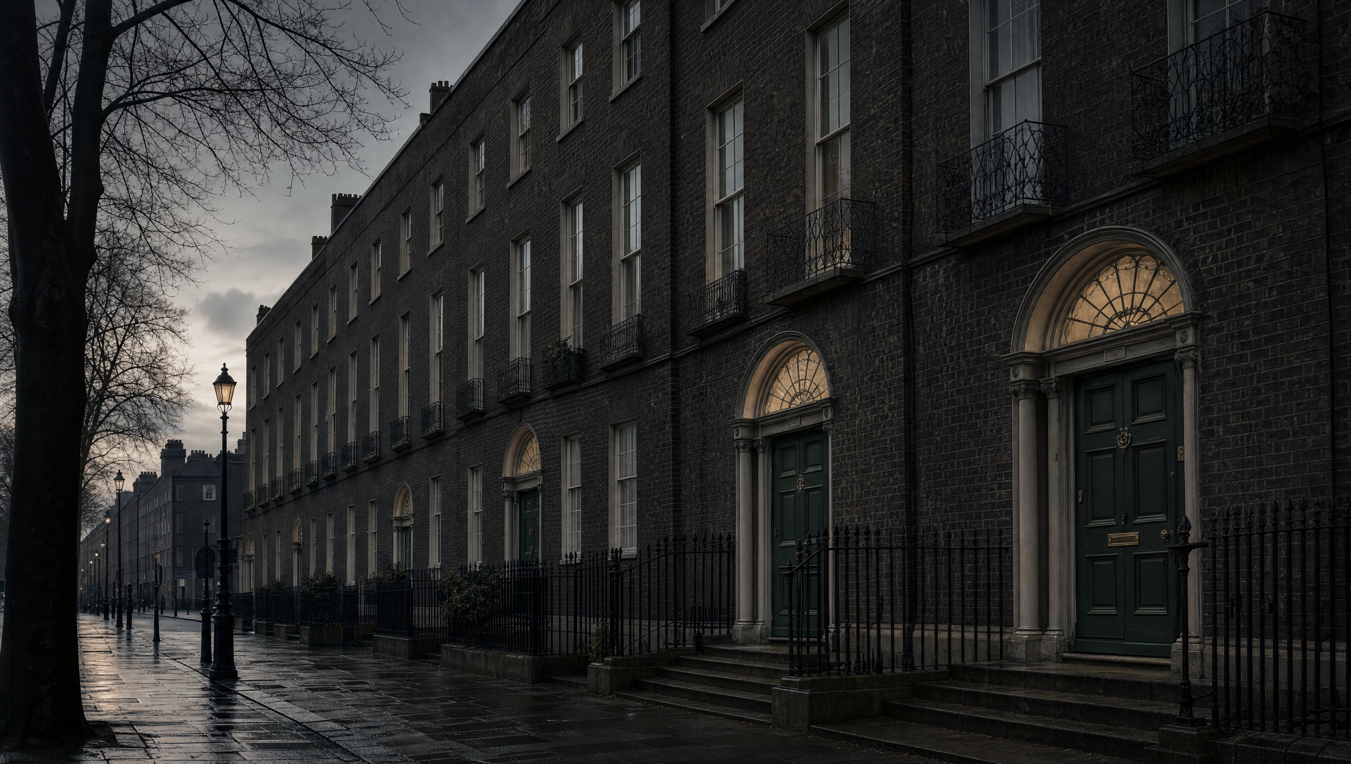 A Georgian terrace at dusk, fanlights above painted doors and wet granite pavement under bare branches