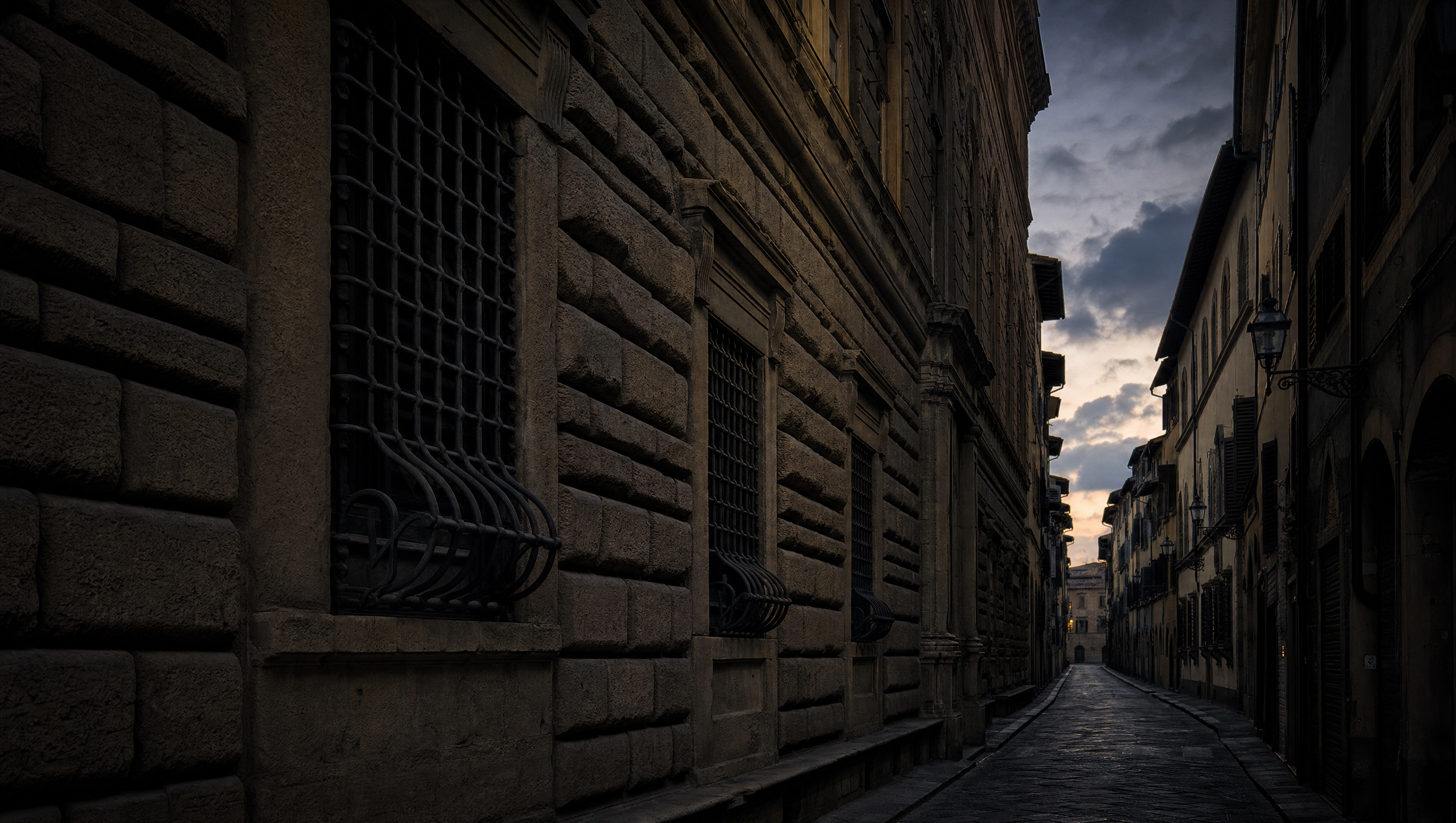 A Florentine street at dusk in the Oltrarno, rusticated stone and deep-set iron-grilled windows