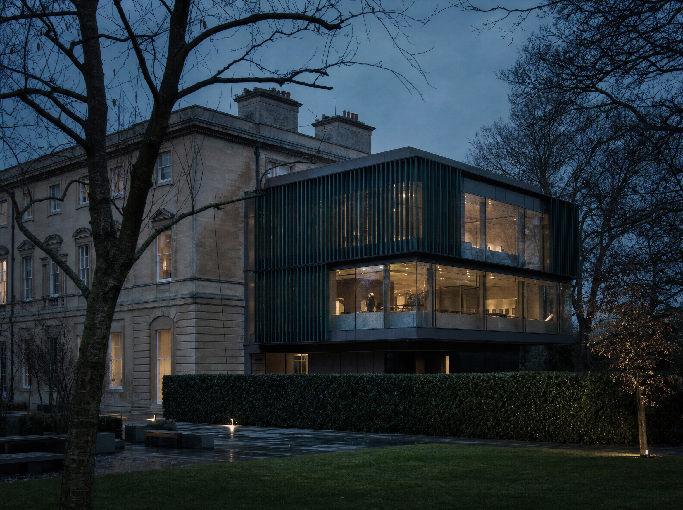 The glass and ceramic-finned extension at the back of the museum, lit from within at blue hour, seen from the gardens