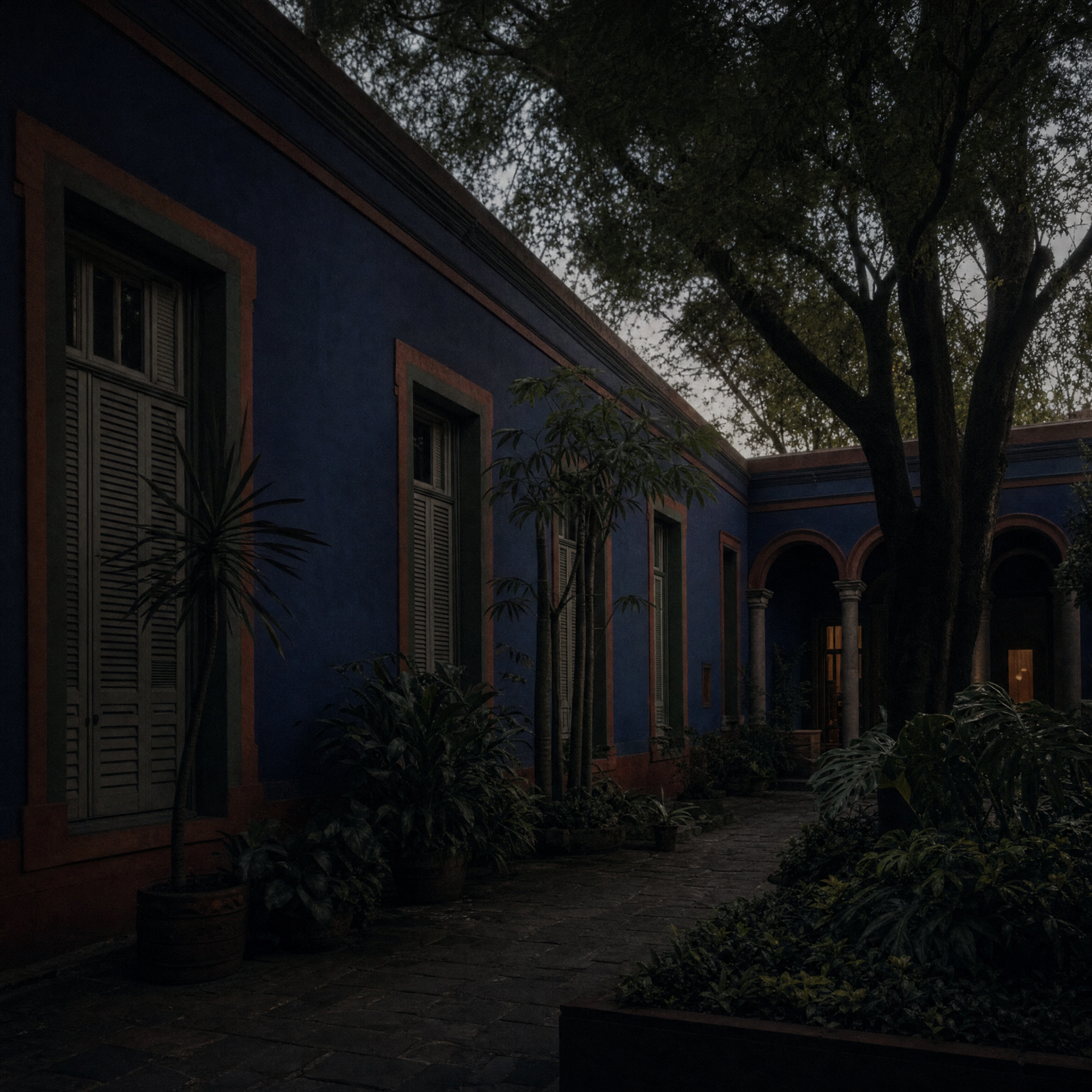 The courtyard elevation of the Casa Azul at dusk, cobalt walls with red-oxide frames and dark planting