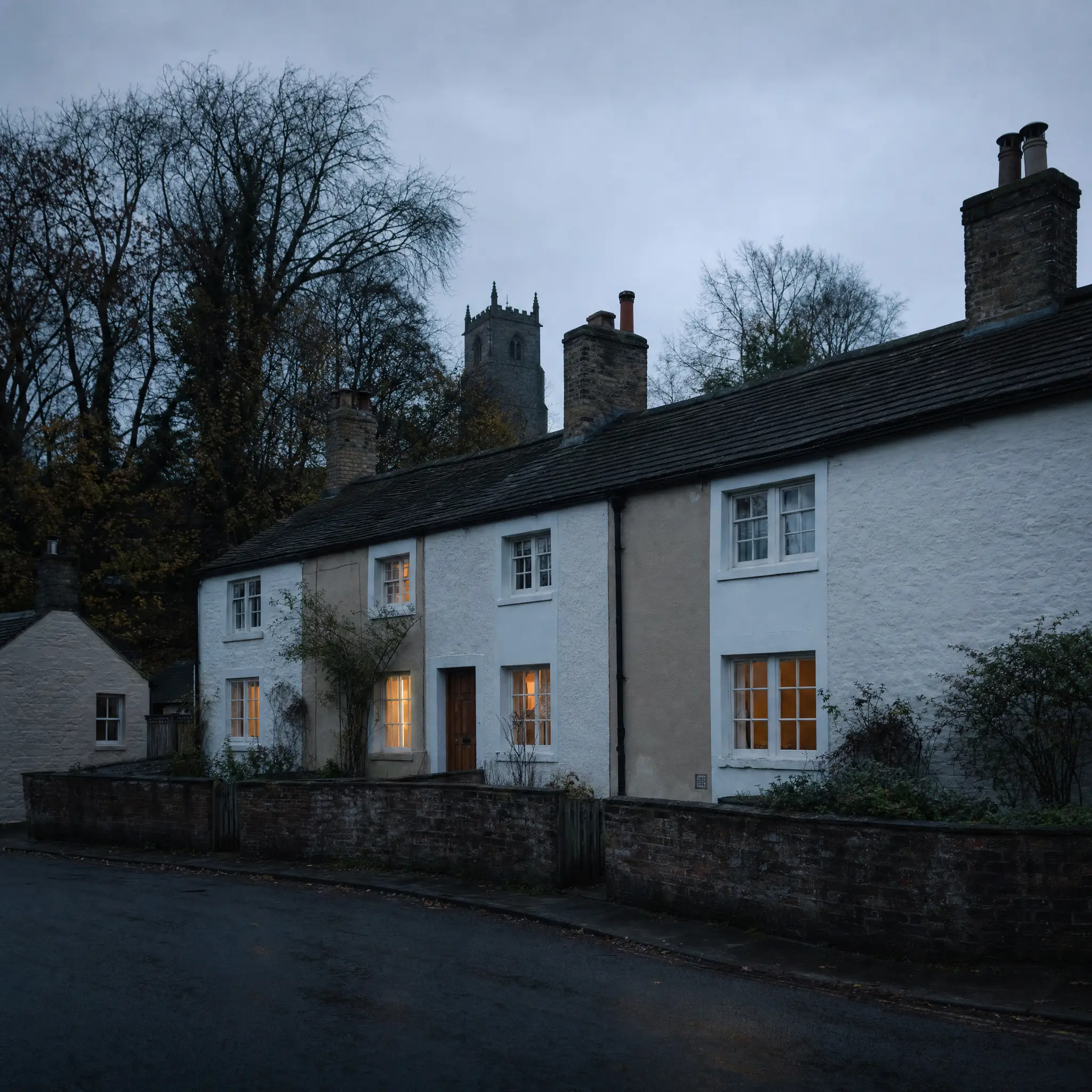 The row of joined cottages on Castle Street at dusk, lit windows, the church tower behind
