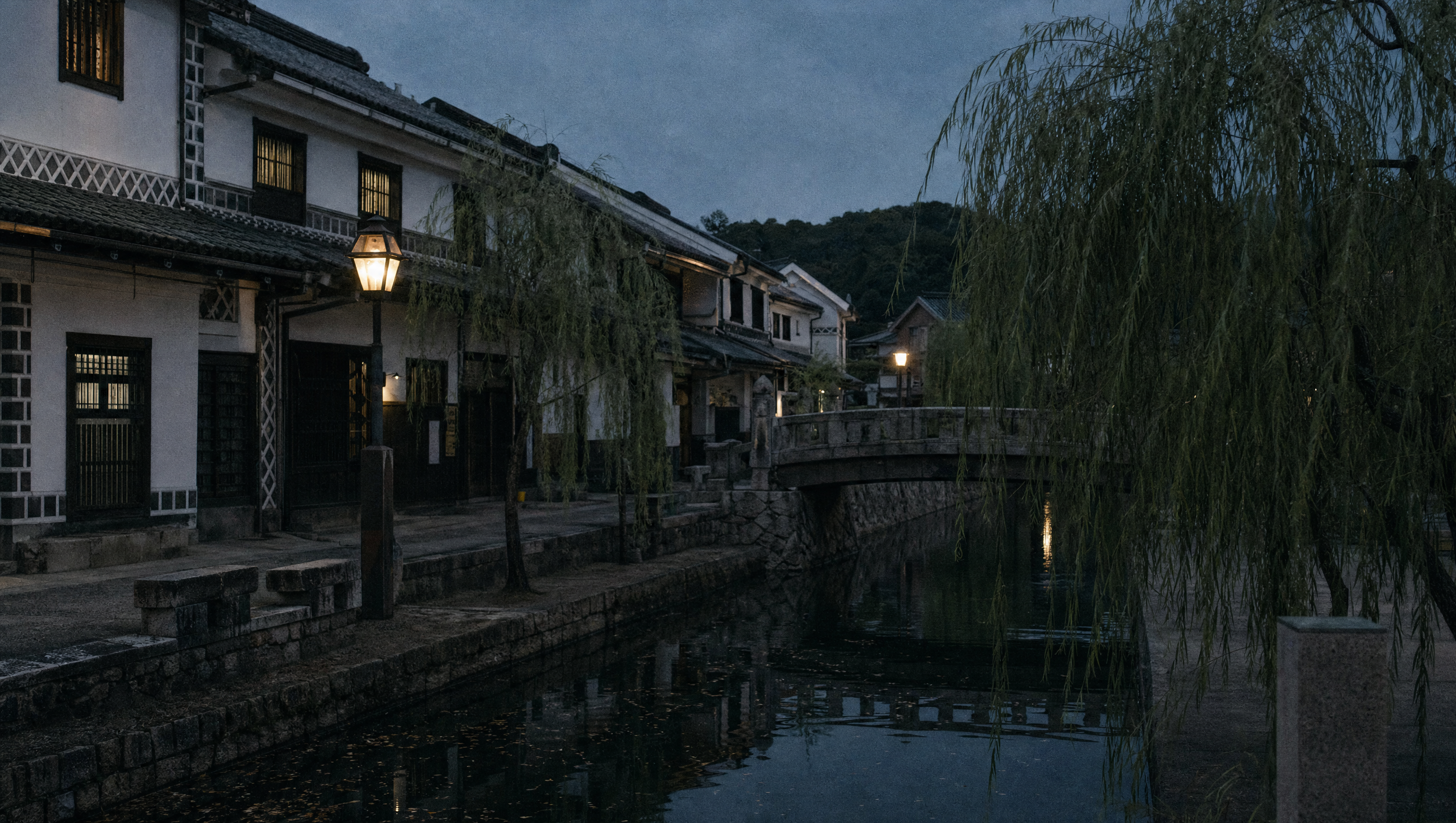 A willow-lined stone canal in a preserved merchant quarter at dusk, white storehouses with black lattice walls