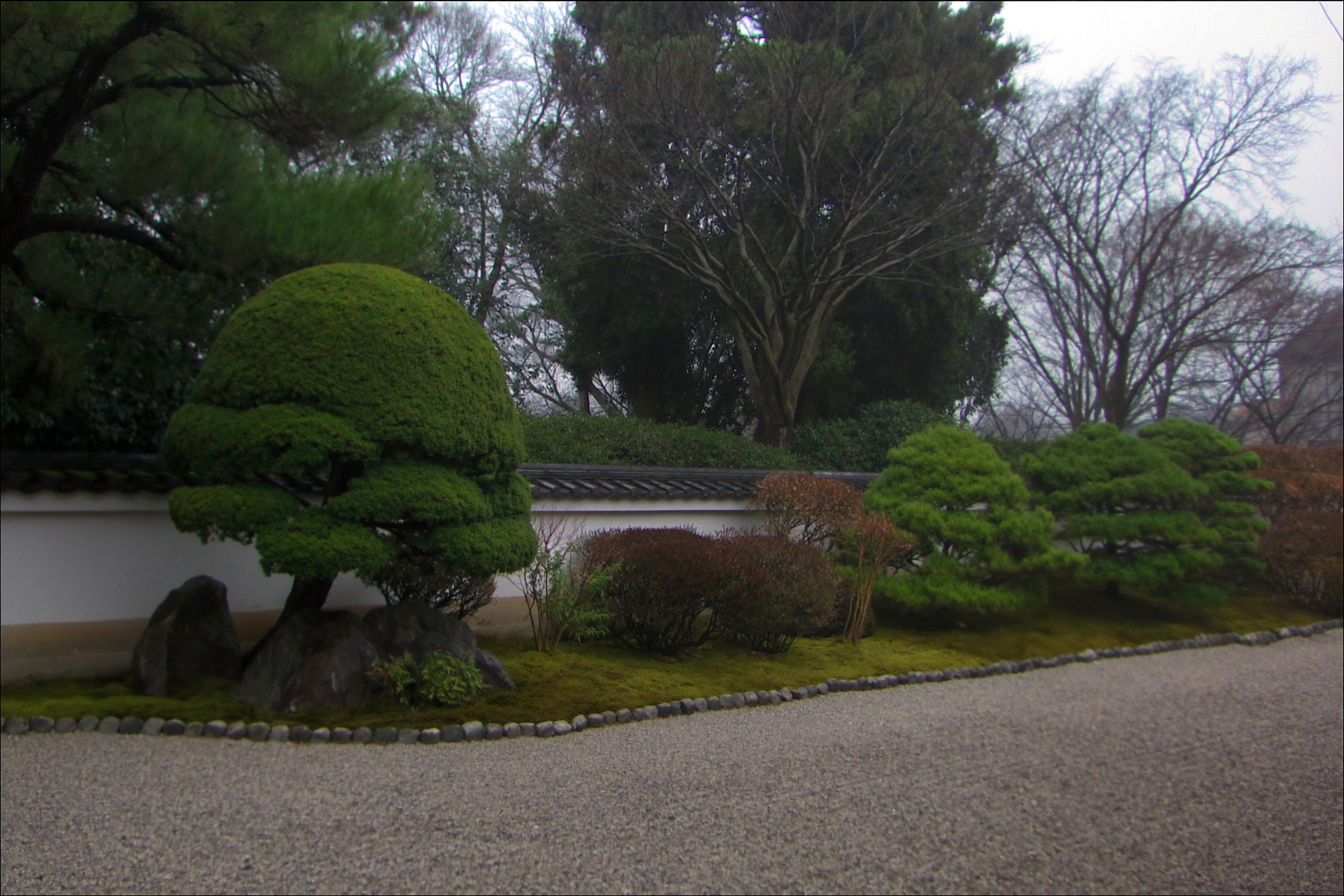 A small raked gravel and moss garden behind an earthen wall