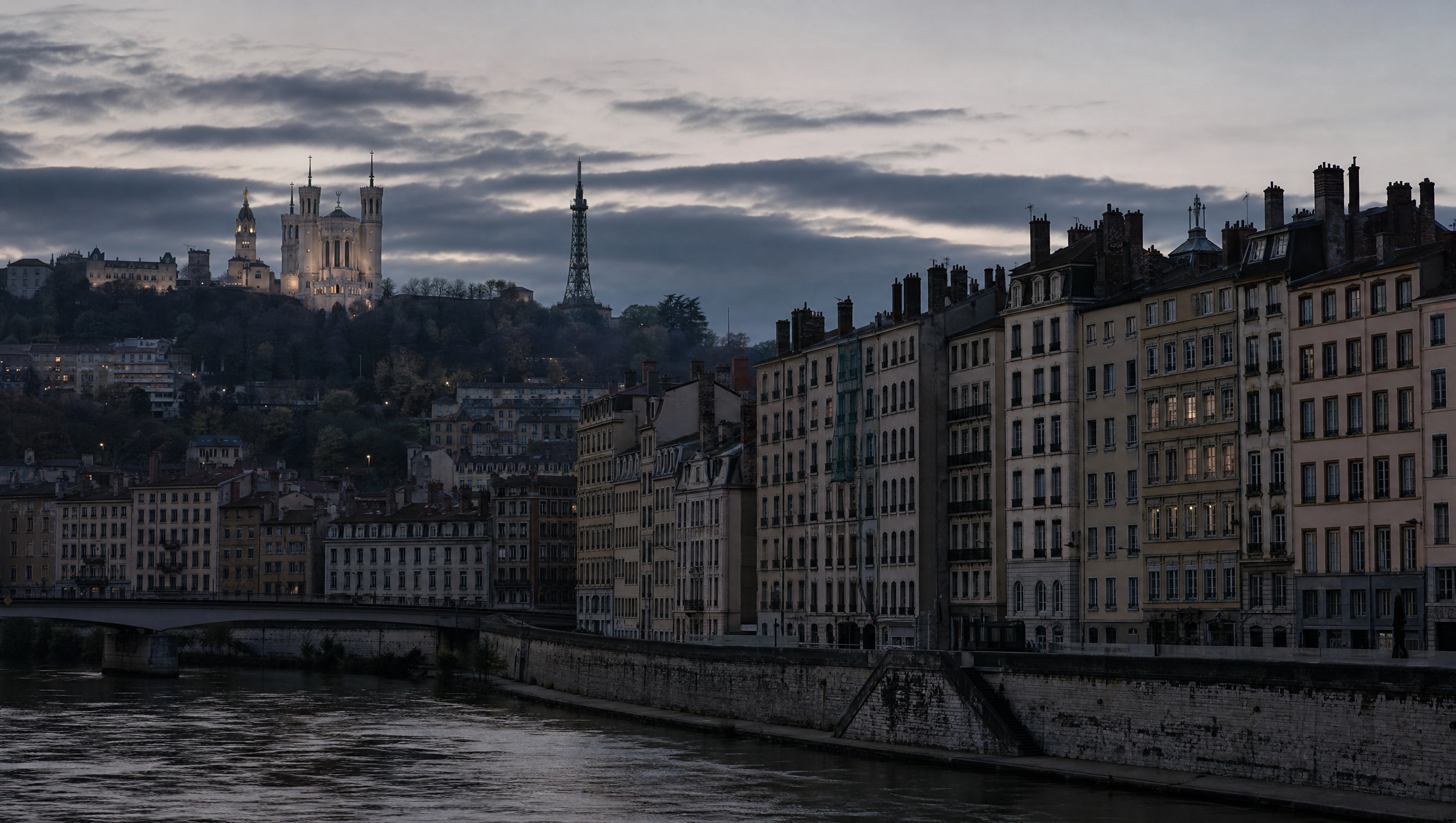 The quays and ranked nineteenth-century facades of Lyon at dusk, the river below and the hill behind in haze