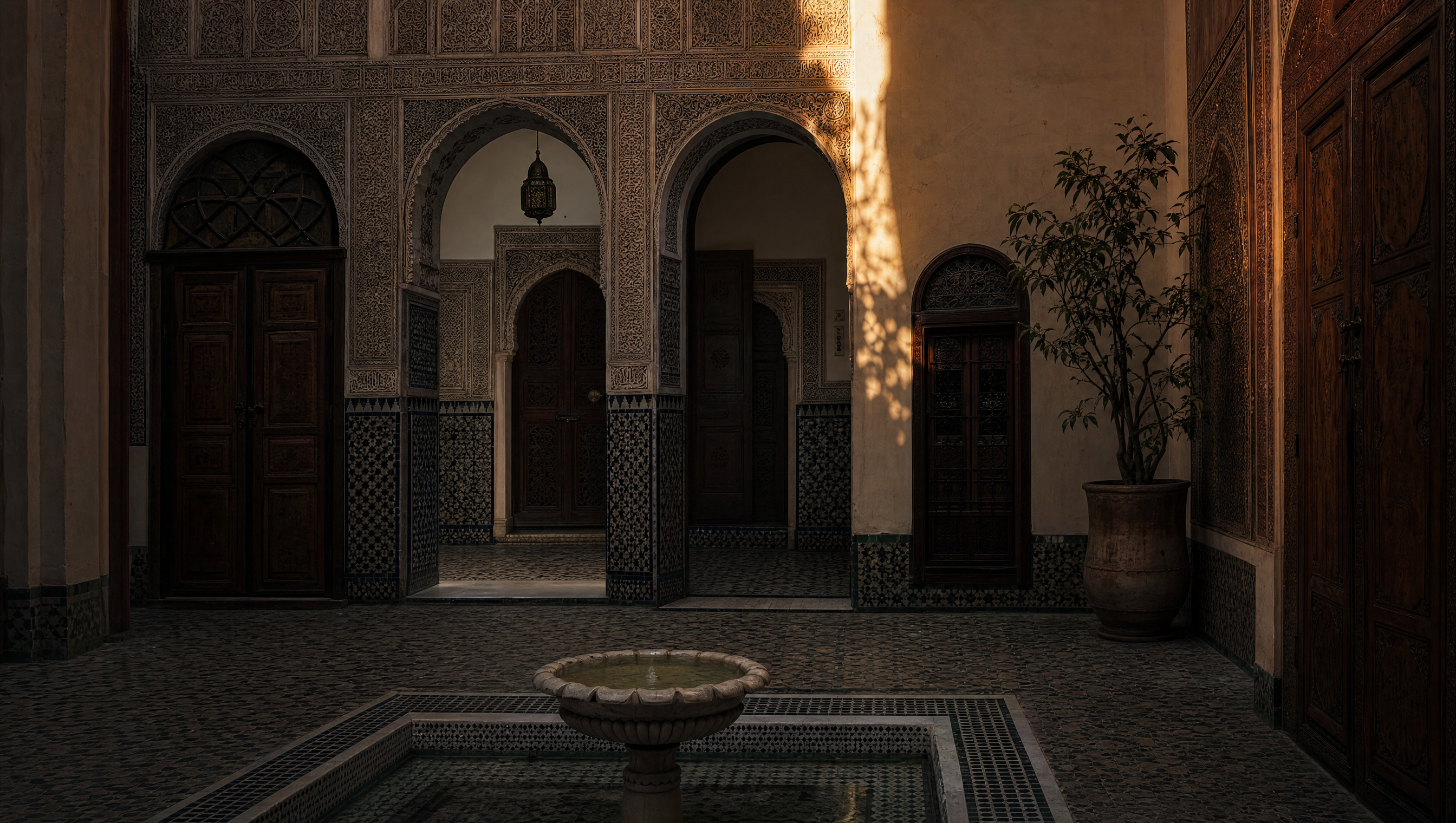 An empty riad courtyard, carved cedar doors and zellij floor, one shaft of late light on the plaster