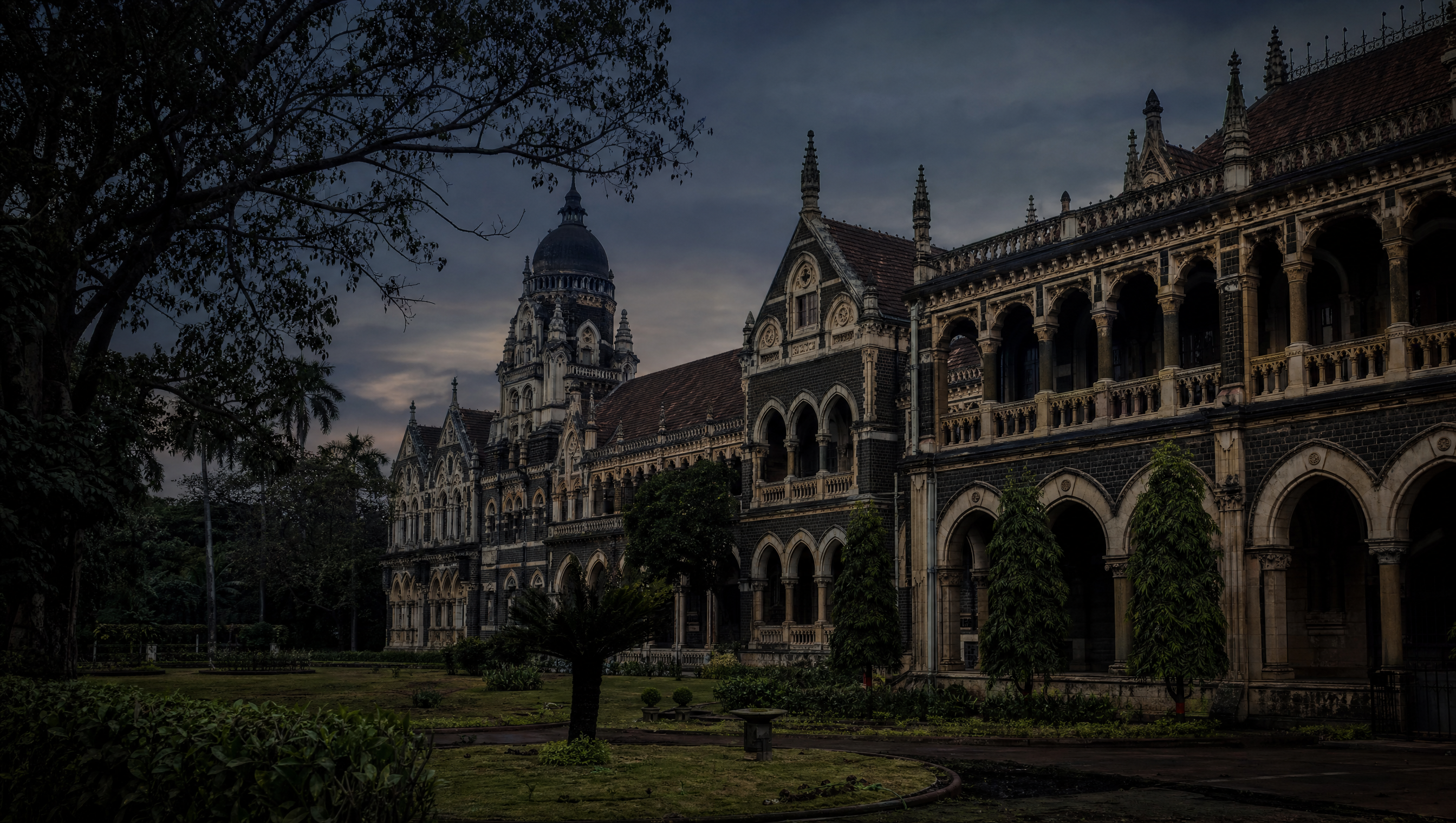 A nineteenth-century stone civic building in Mumbai seen across an empty garden at dusk