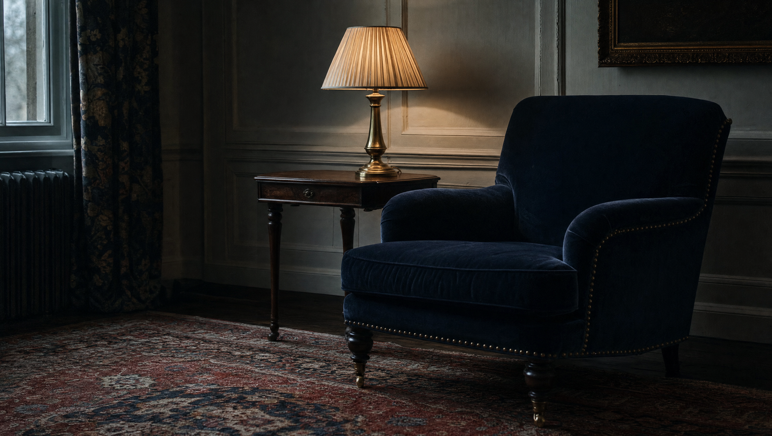 A brass lamp on a walnut side table beside the navy armchair