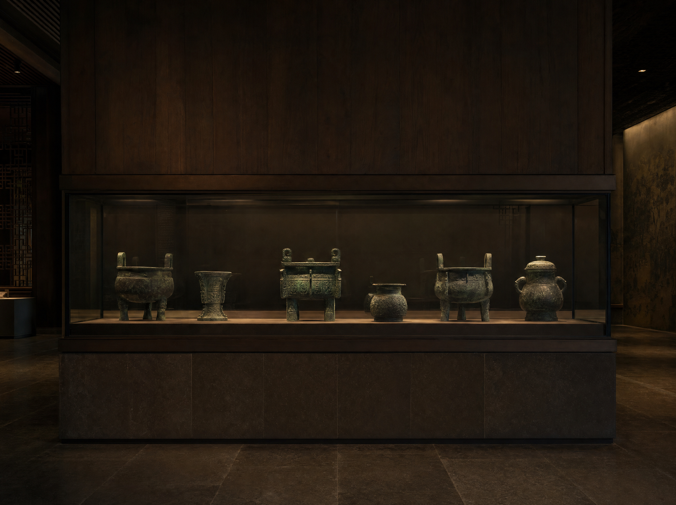 A low gallery vitrine of Chinese archaic bronze vessels lit softly from above