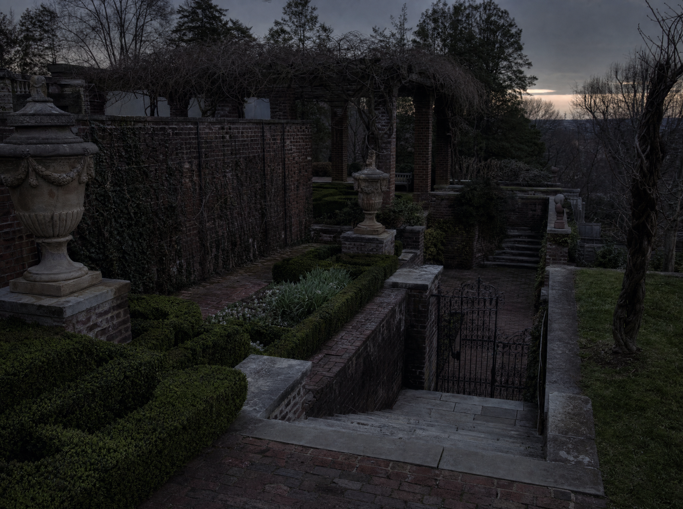 A walled brick terrace with clipped box parterres and worn stone steps descending to a lower terrace