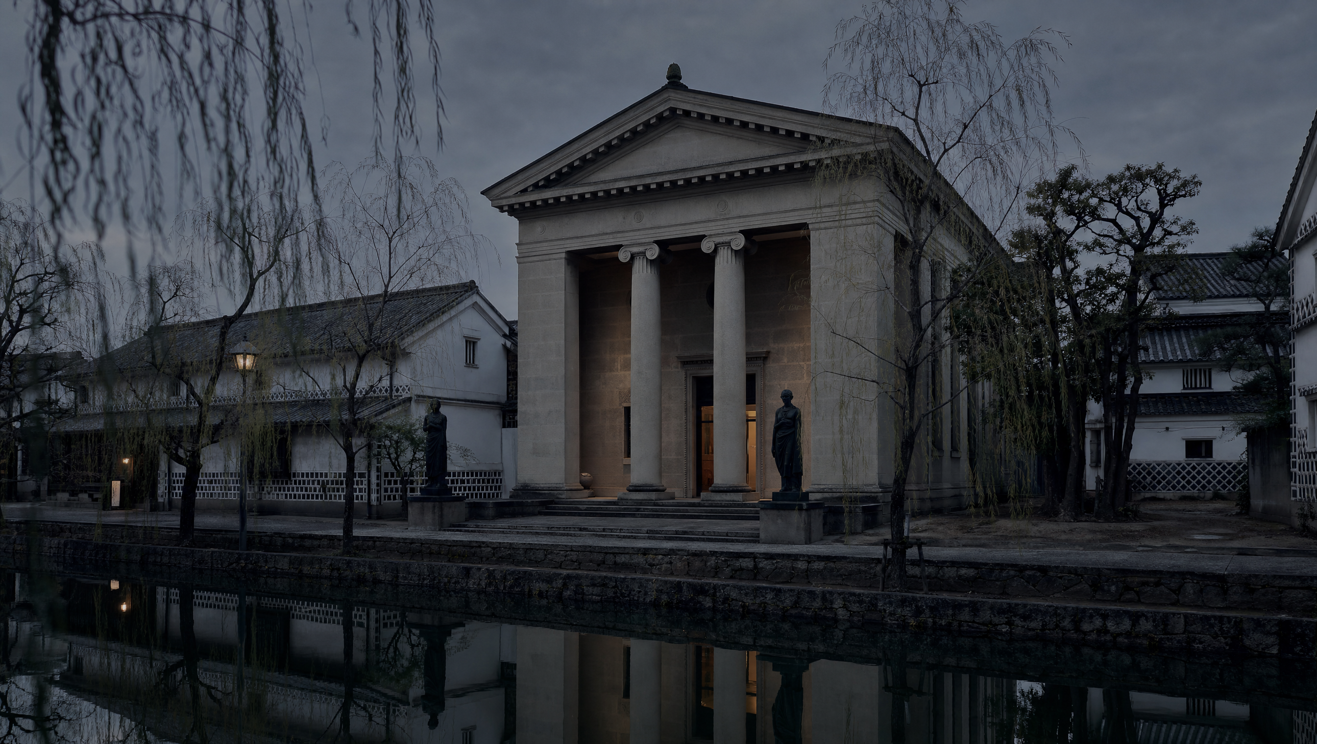 The Ionic stone portico of the Ohara Museum of Art standing on the Kurashiki canal at dusk, bronze figures flanking the entrance, white storehouses either side