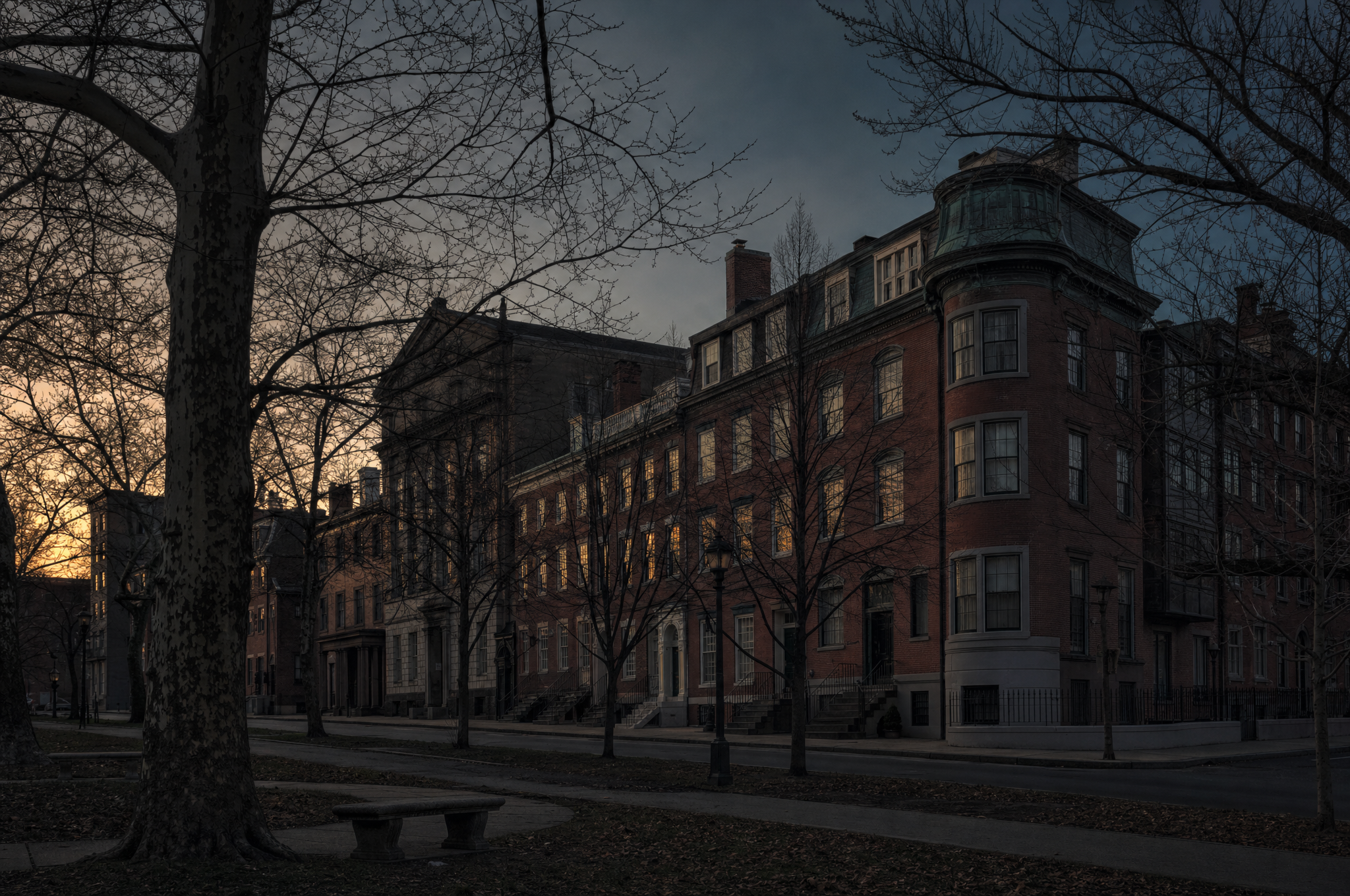 A Philadelphia block at dusk, red brick and stone with bare trees along a parkway