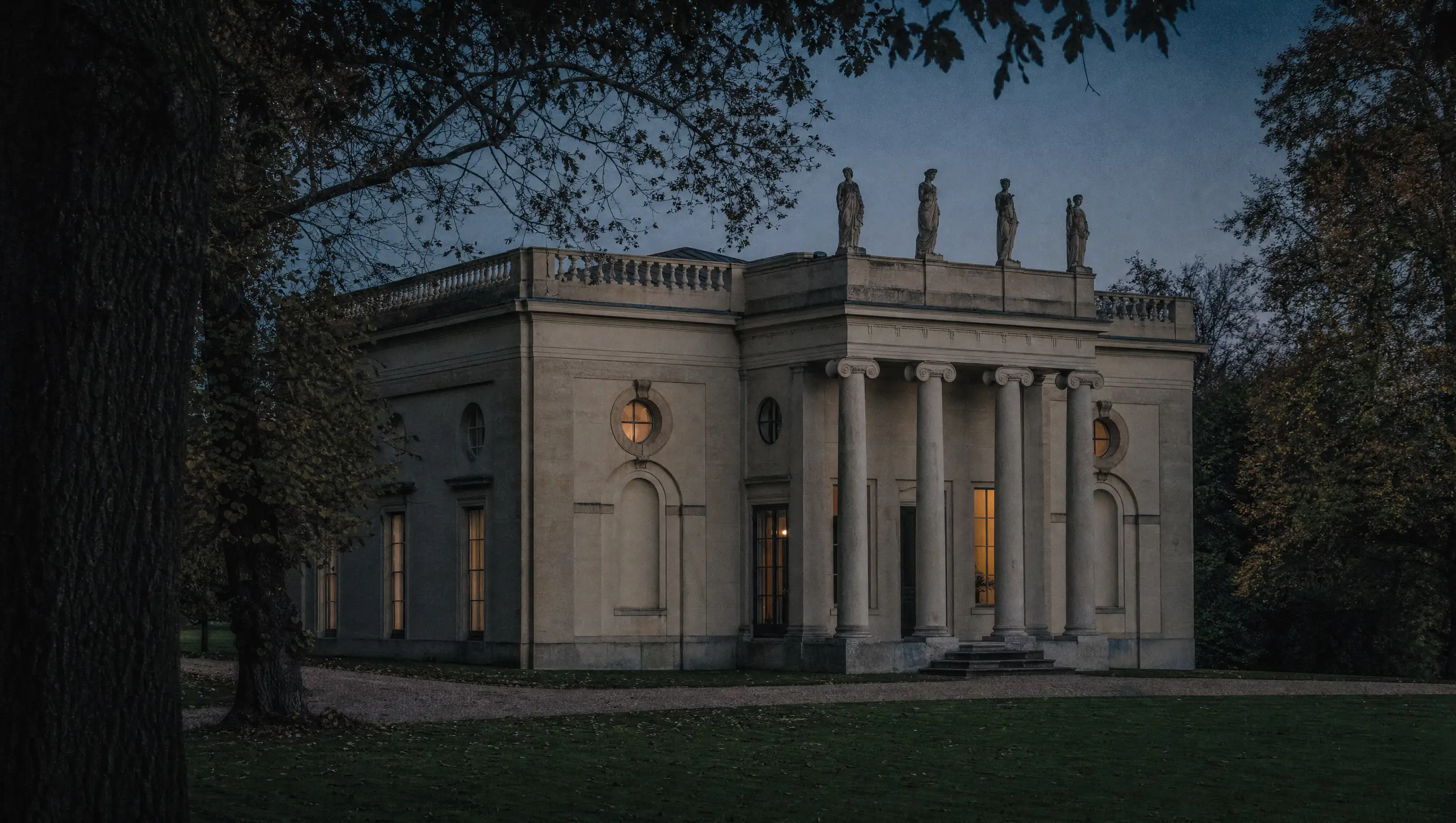 The columned entrance front of Pitzhanger Manor at dusk, statues on the parapet above