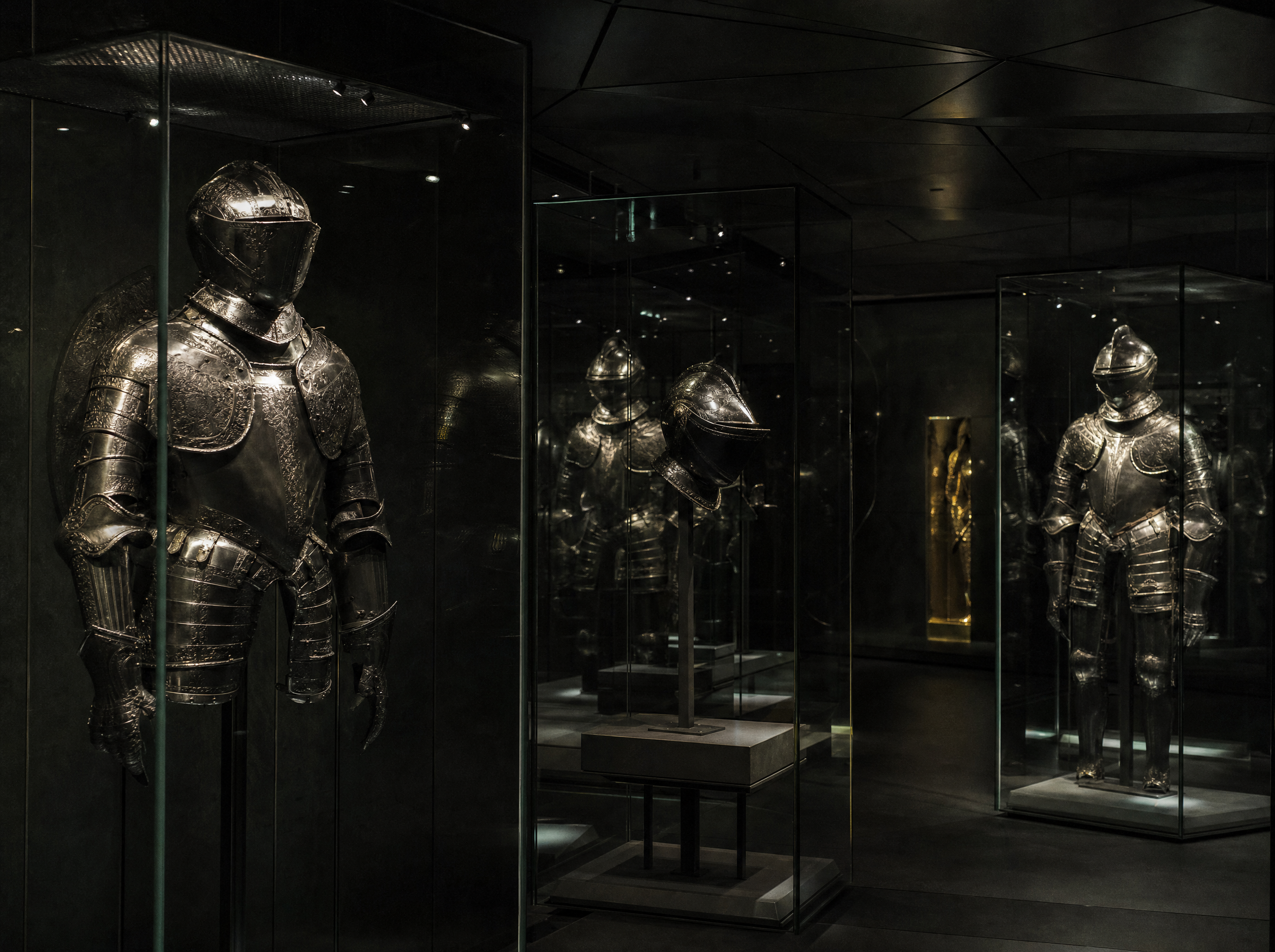The armoury, armour lit out of near-darkness on slim steel mounts