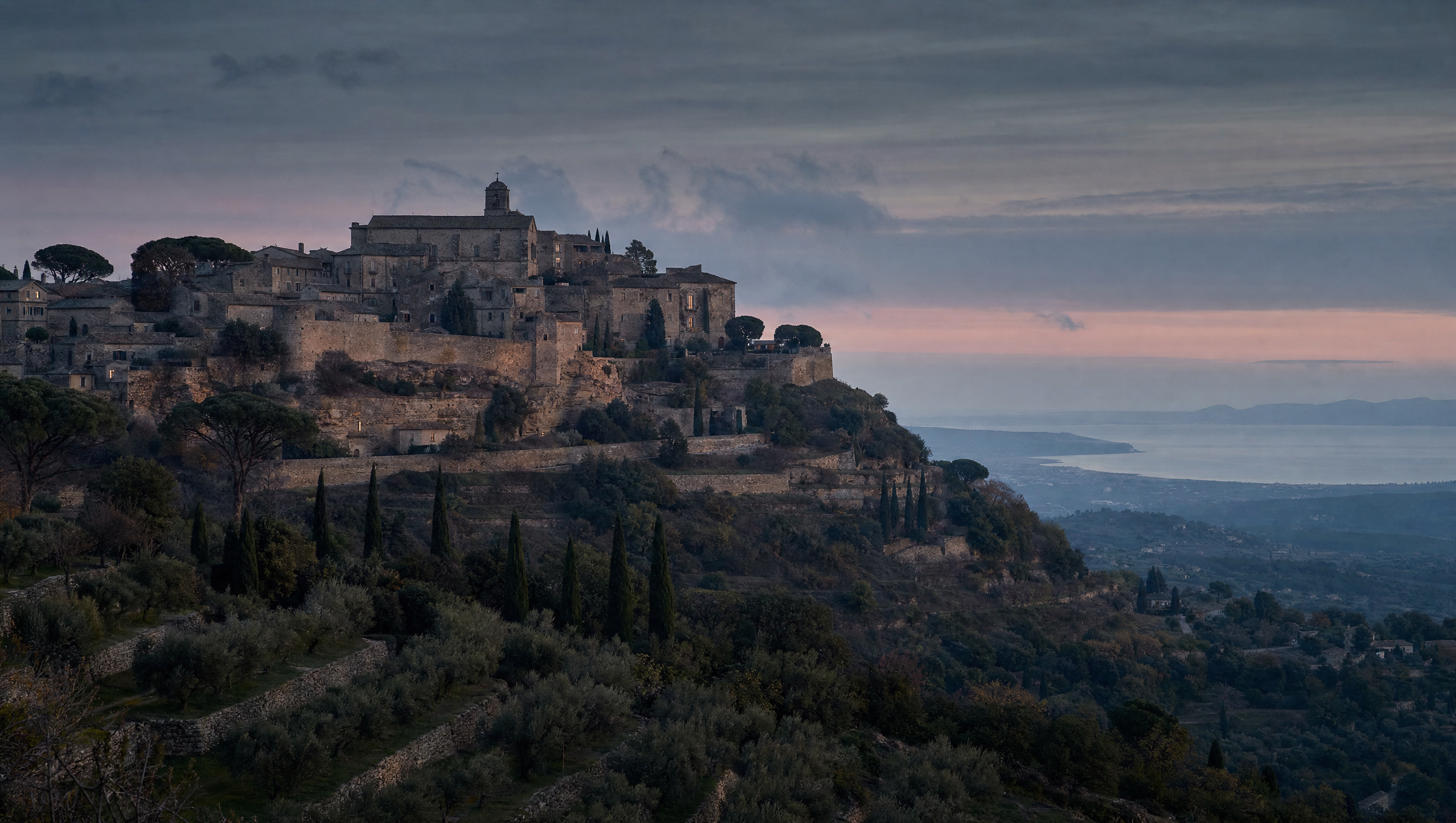 A fortified hill village in Provence at dusk, terraced slopes, umbrella pines and tiled roofs