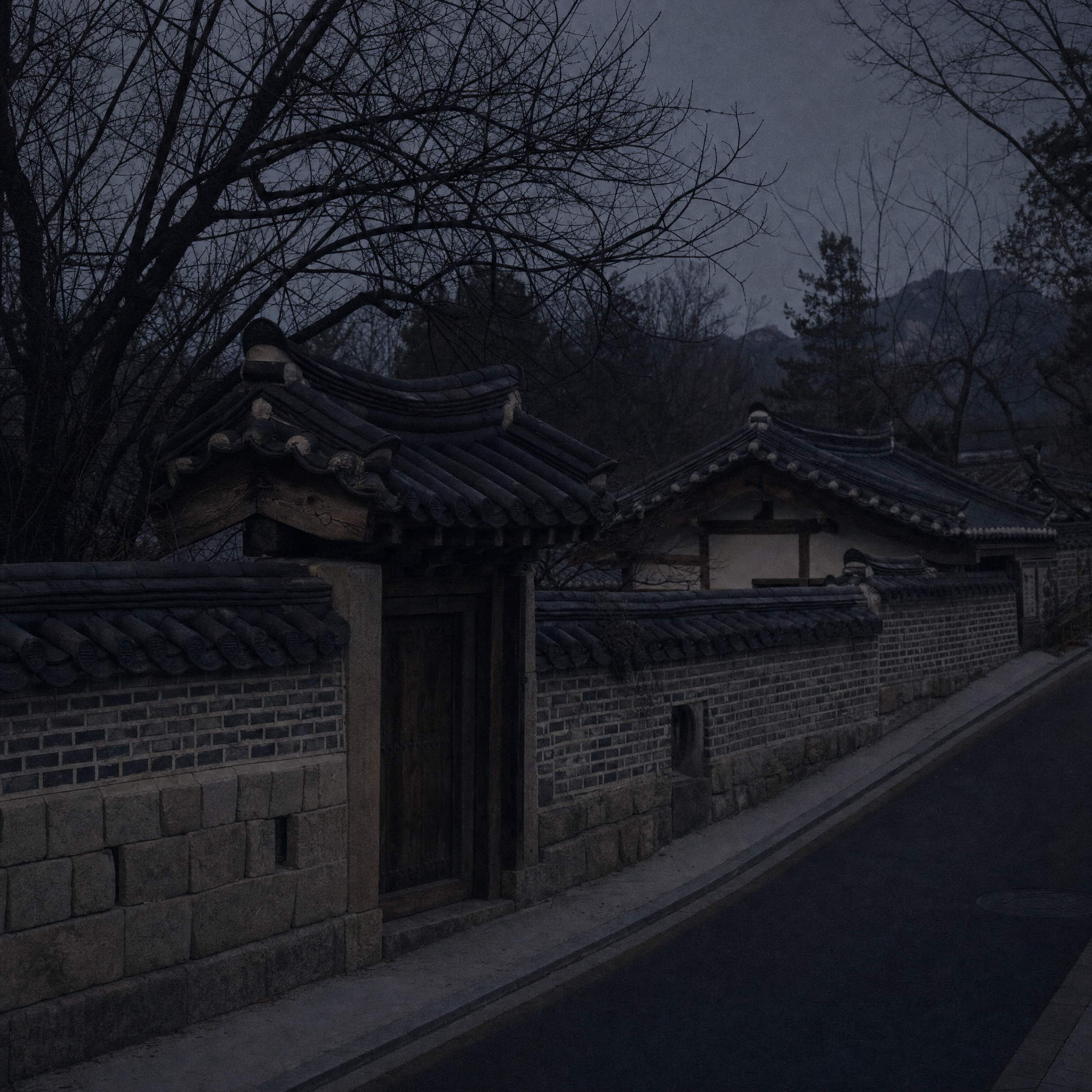 A quiet lane of tiled roofs and old walls under bare trees at dusk